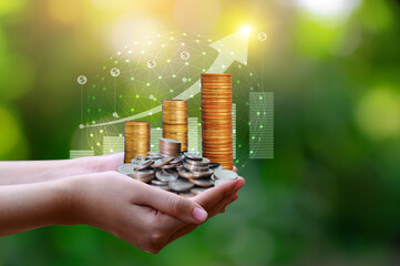 Close up of hands holding stacked gold coins with growth graph and global network on green bokeh background.