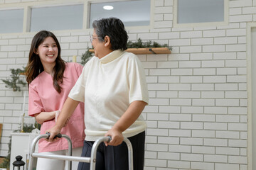 Fototapeta premium Asian nurse assisting senior woman walking with walker at home, rehabilitation support, elderly care service, physical therapy, caregiver helping patient mobility, healthy aging concept.