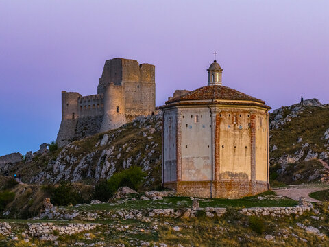 Aerial view of the medieval fortress of Rocca Calascio and the octagonal church of Santa Maria della Pieta under a twilight sky in Calascio, Abruzzo, Italy.