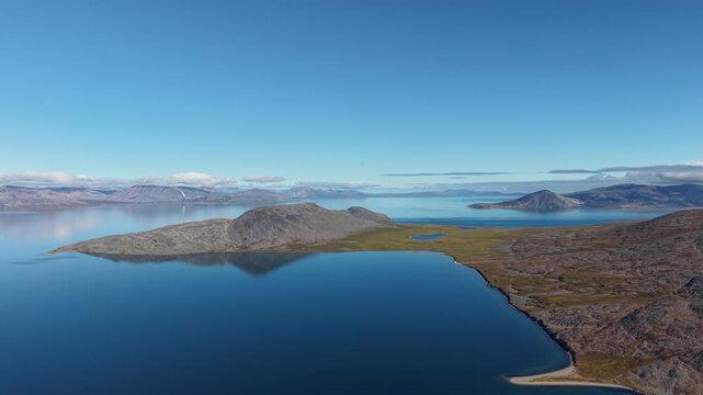 Gentle drift over Rumilet Bay in Chukotka at late evening. Rocky peninsula meets calm blue water under clear sky. Early autumn wilderness scenery for cinematic travel, tourism and exploration projects