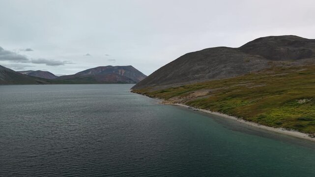 Aerial footage follows Penkigney Bay shoreline near Provideniya. Chukotka coast faces the Bering Strait with tundra slopes and cold water. Early summer morning with steady tracking move