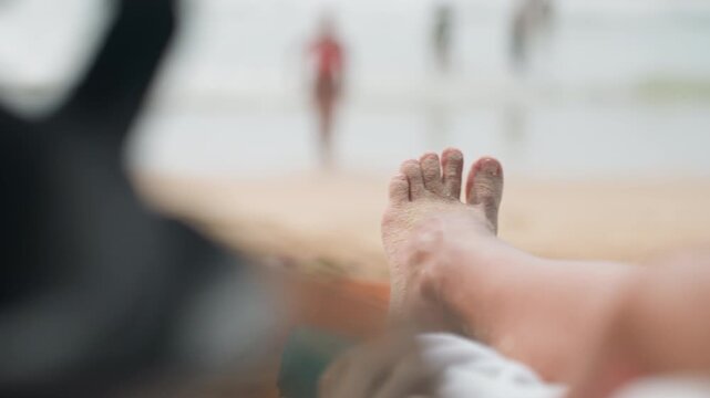 Relaxed toes resting on peaceful sandy shores. Tranquil coastal scene with blurred swimmers and soothing atmosphere. Calm beach setting where gentle waves meet sandy toes and peaceful surroundings