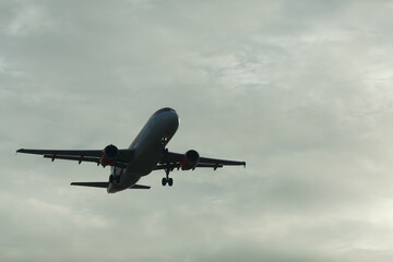 Obraz premium Commercial aircraft approaches landing amidst a cloudy sky, showcasing the airplane's silhouette against the backdrop of the evening light