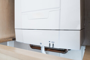 Detailed view of a newly fitted gas central heating boiler seen located in a kitchen cupboard. Part...