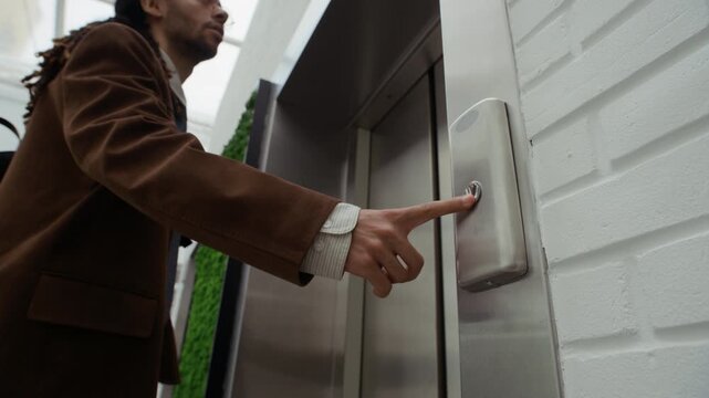 Medium low angle shot of stylish young biracial office worker in suit pressing elevator button, rushing to get on time for work in high rise business center