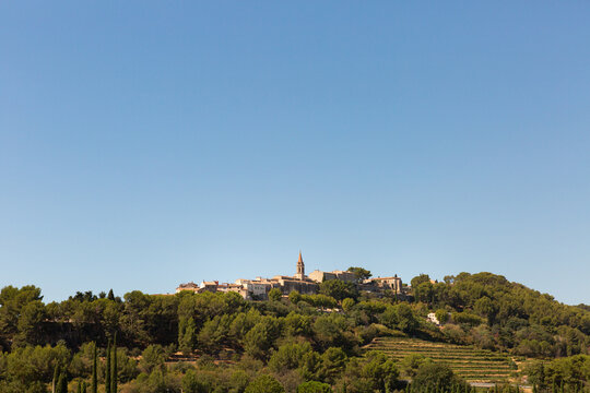 Vue en contre-plong&eacute;e du village proven&ccedil;al de La Cadi&egrave;re d&rsquo;Azur, village m&eacute;di&eacute;val perch&eacute; sur une colline avec son &eacute;glise au centre, entour&eacute; de vignes, pins et cypr&egrave;s, grand ciel bleu, sud de la France