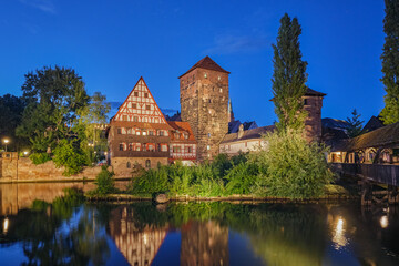Fototapeta premium Panoramic night view of the lit medieval architecture and towers reflecting in the river water in Nuremberg, Bavaria, Germany.