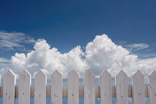White picket fence against a vibrant blue sky with fluffy white clouds in the background