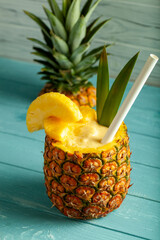 Pineapple cocktail presented in a hollowed pineapple with a straw and pineapple slice, placed on a...