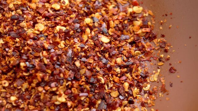 Macro shot of crushed cayenne and red chili pepper flakes with seeds. Scattered spices inside a rustic bowl. Healthy cooking ingredients