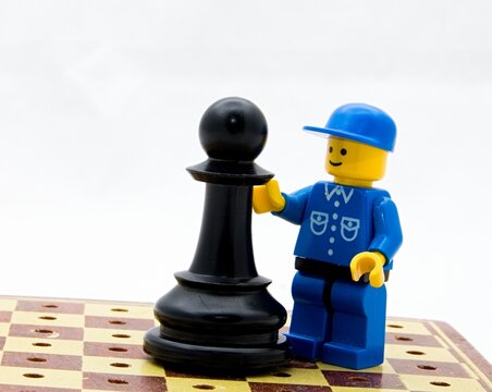 A lego figurine with a chess piece on a small chess board