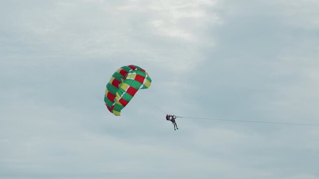 Parasailer above island horizon sunrise calm sky, colorful canopy drifts over distant island silhouette, slow leisure motion, tethered rider suspended above coastal water, gentle breeze, soft cloud