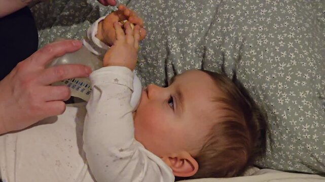 Adorable baby lies comfortably on a bed drinking milk from a bottle during a peaceful feeding at home.