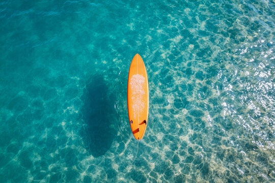 Surfboard aerial top view orange floating in the clean and clear sea water wave