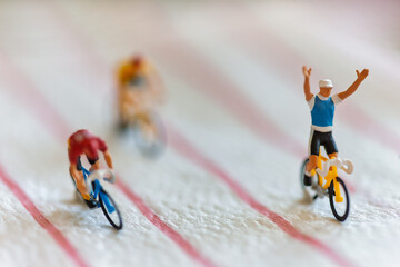 Obraz premium Miniature Cyclists Representing Corporate Success and Financial Growth with the leader raising his arms in victory