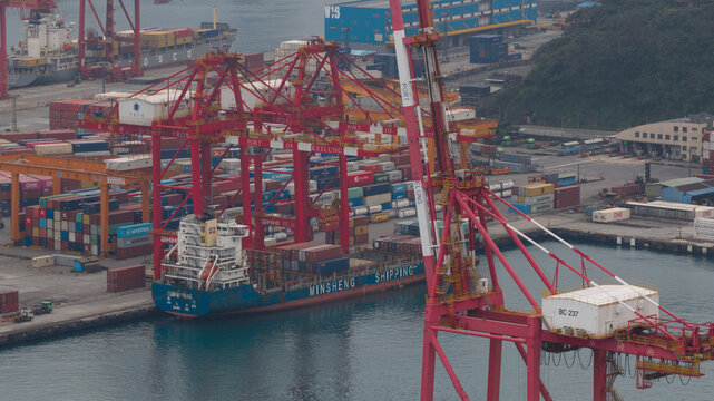 Keelung City, Taiwan - 20 February 2026: Aerial view of stacked shipping containers casting long shadows, with giant red cranes towering over the scene at Zhongshan 4th Road.
