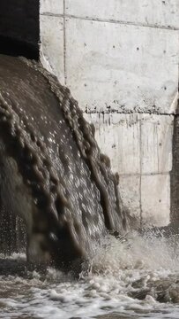 Vertical video: Outfall releasing thick flow for drainage, lobes traveling down and creating foam