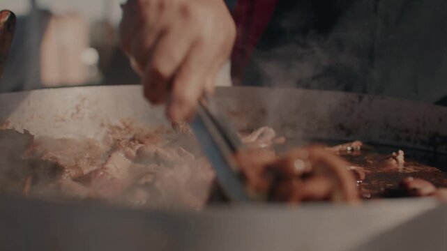 Sizzling Cooking Meat Being Stirred With Tongs in Large Pan on Grill