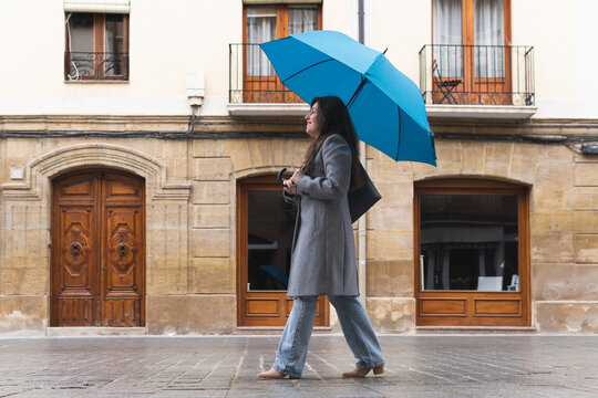Woman walking with blue umbrella on rainy city street