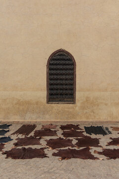 View of leather hides spread out to dry in the sun on the ground below a barred window in a textured wall, Marrakesh, Marrakesh-Safi, Morocco.