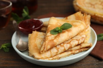 Tasty crepes with jam and mint leaves served on wooden table, closeup © New Africa