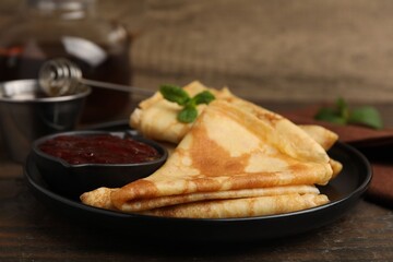 Tasty crepes with mint leaves and jam served on wooden table, closeup © New Africa