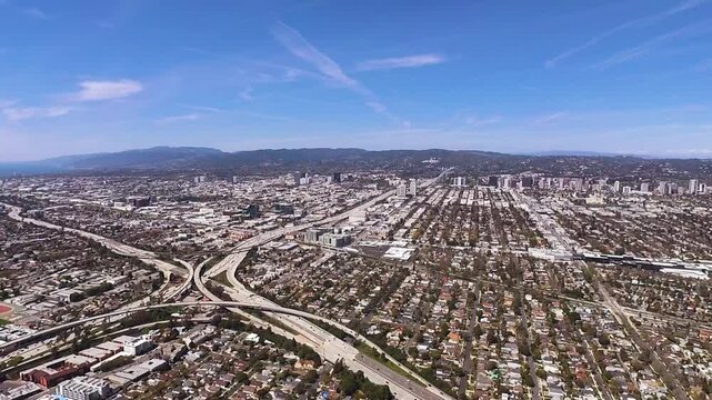 An aerial view of a major freeway interchange (I-10 and I-405) in West Los Angeles with clear view of Santa Monica out to the Pacific Ocean.