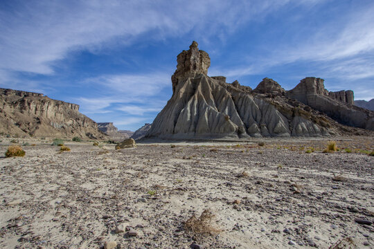 View of rugged rock formations rising from the arid landscape under a vast blue sky dotted with wispy clouds, creating a stark contrast, Hingol National Park, Balochistan, Pakistan.