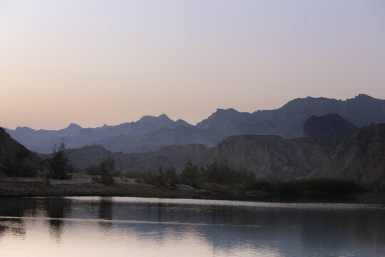 View of serene waters reflecting the dusky sky and rugged mountain silhouettes, a tranquil landscape in Hingol National Park, Balochistan, Pakistan.