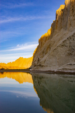 View of golden cliffs reflecting in the tranquil waters under a blue sky, a serene contrast of colors and textures, Hingol National Park, Balochistan, Pakistan.