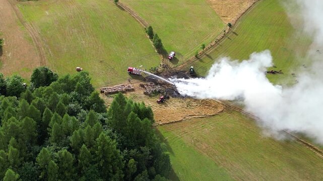 Aerial view of firefighting efforts in a rural landscape, showcasing fire trucks and smoke billowing from a controlled burn, with dynamic camera movement