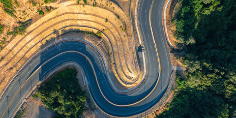 Aerial view of Golden sunset light glowing over a winding mountain road on a high ridge in Nan Province, Thailand, creating a dramatic landscape of curves and towering peaks. © Narong Niemhom