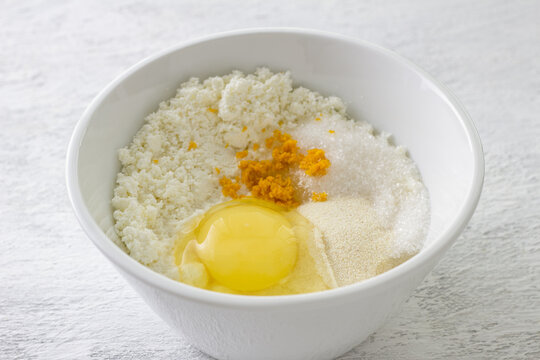Ingredients for ricotta cheese filling in white bowl with raw egg orange zest semolina and sugar on kitchen table