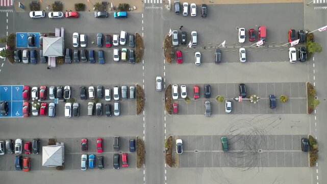 Aerial view of busy parking lot near shopping center, showcasing various parked vehicles, camera pans across scene highlighting parking dynamics and space utilization