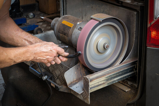 Farrier works on motorised grinding wheel with sparks to refine horseshe in workshop