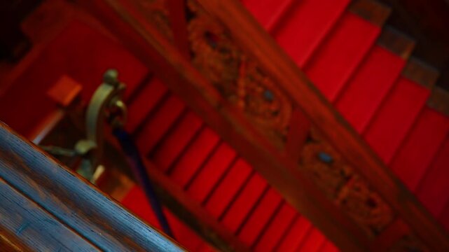 Detail of ornate wooden staircase with red carpet. High angle close-up of decorative wood banister and stairs covered in vibrant red carpeting in a classic building.