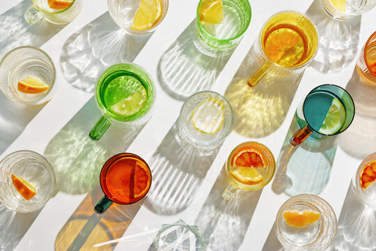 Vivid Glasses with cold detox water as summer still life pattern, shadow and sunlight refraction, closeup glass cups of infused fruit water, slises of lemon, orange, healthy summer drink