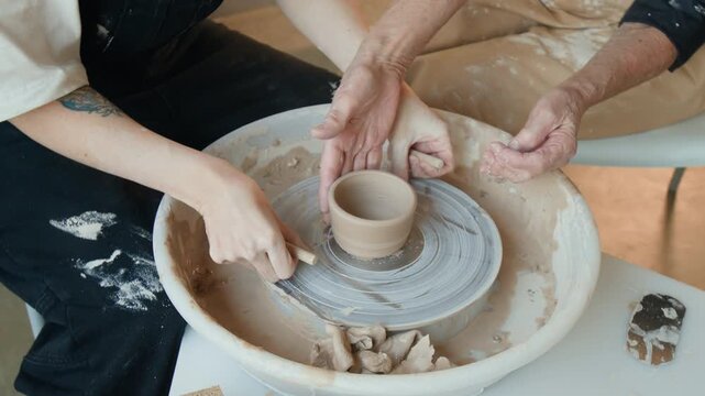 High angle shot of two unrecognizable women using thread to trace bottom of ceramic piece on potters wheel in workshop