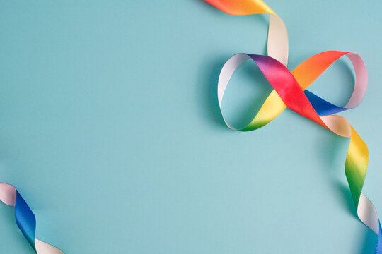 Infinity Satin Ribbon in Shape of Rainbow on Light Blue Background. Autism Acceptance and Neurodiversity Concept