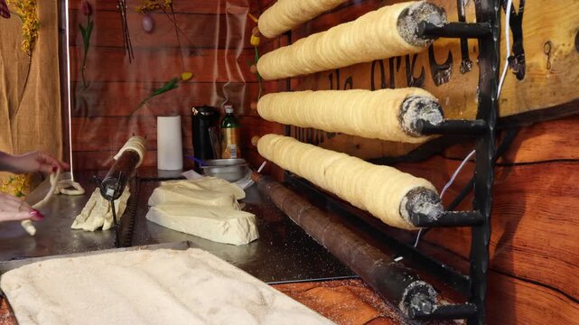 Traditional chimney cake baking process dough wrapped on wooden rollers sugar coating cooking over heat street food preparation sweet pastry fresh dessert market scene