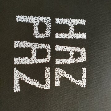 Mensaje HAZ PAZ, texto hechos con trocitos de papel blanco, estilo mosaico sobre fondo negro.