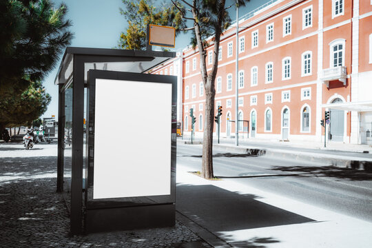 Blank bus stop billboard mockup on city street, vertical advertising display template with copy space at modern shelter in sunny urban scene near pastel building facade