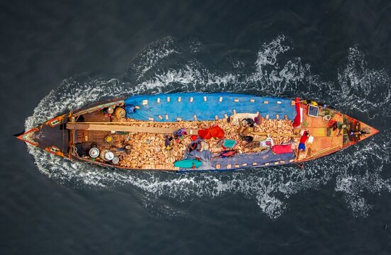 Aerial view of a boat laden with goods slicing through the dark waters, creating a vibrant contrast of colors and textures, Dhaka, Dhaka Division, Bangladesh.