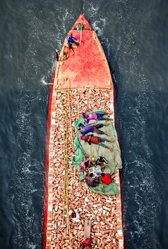 Aerial view of a vibrant boat carrying people and cargo, creating a striking contrast against the dark waters, Munshiganj, Dhaka Division, Bangladesh.