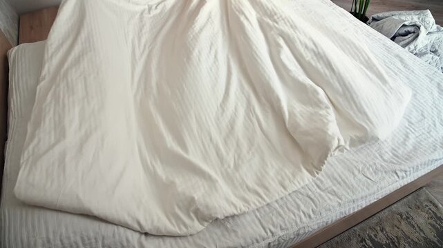 Person arranging white bedding on bed, visible mattress and bedroom setting