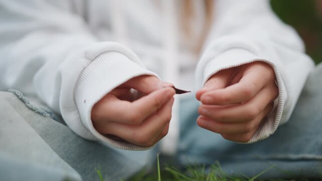 Hands gently touch grassy outdoor scene. Delicate hand movements amidst nature during serene outdoor moment. Fingers softly fidget with grass and fabric in tranquil outdoor meadow environment