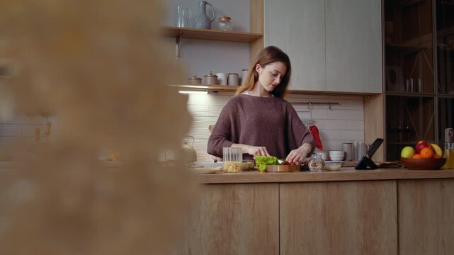 Young woman prepares daily lunch checking tablet in home kitchen