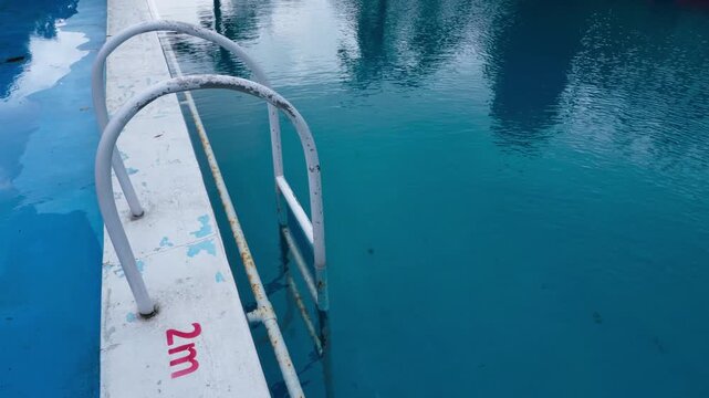 Footage of calm blue swimming pool water with metal ladder and gentle ripples. Minimal outdoor scene with copy space, ideal for travel, relaxation, resort lifestyle, and summer background use.