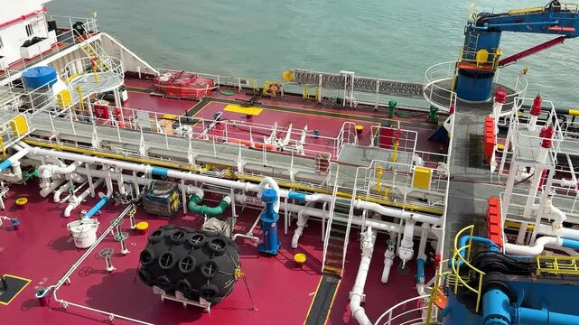 Workers are busy on the deck of a large tanker in a harbor. They operate machinery and handle equipment while the ship is docked. Tasks include loading and unloading cargo.