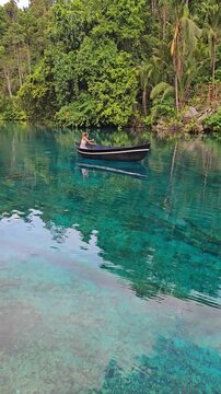 Woman floating on boat in lake with crystal blue fresh water in Sulawesi, Indonesia